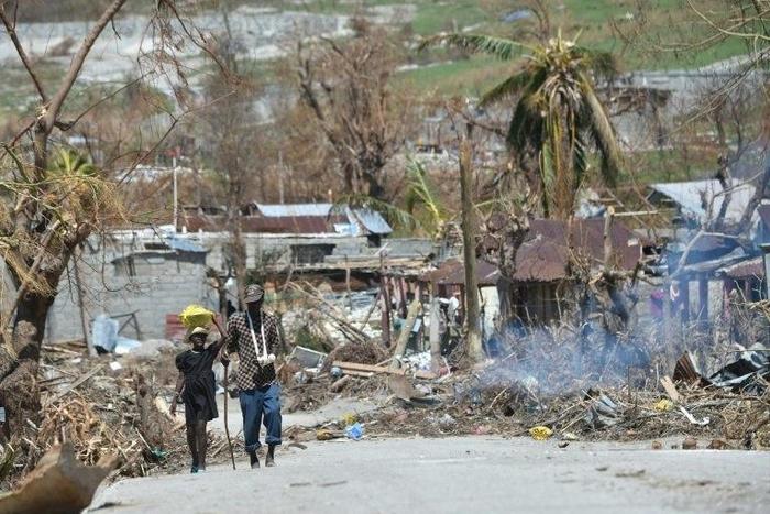 People walk down a debris covered street in the commune of Port-a-Piment, in Les Cayes, in southwest Haiti, on October 11, 2016