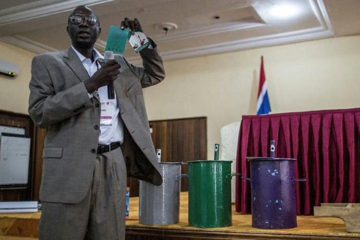 An IEC (Independent Electoral Commission) official shows an electoral document of incumbent president Yahya Jammeh next to the ballot boxes with the three parties colours on November 28, 2016