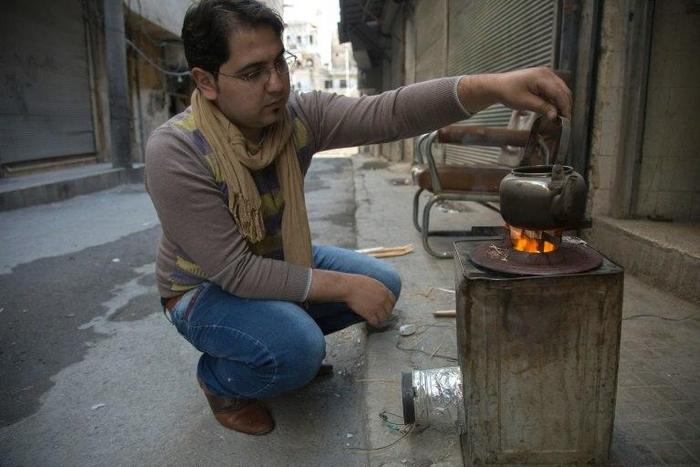 Khaled Kurdiyah, who runs an internet cafe, uses a metal container outfitted with a fan to create a highly-controlled fire to replace rare gas-fired stoves while using minimal firewood, in besieged Aleppo