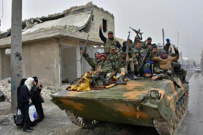 Syrian pro-government forces cheer on a military vehicle driving past residents on November 30, 2016 fleeing a former rebel-held district of eastern Aleppo, northern Syria which was retaken by the regime forces last week