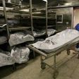 Morgue attendant is seen pushing a corpse lying on a gurney,