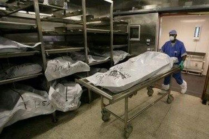 Morgue attendant is seen pushing a corpse lying on a gurney,