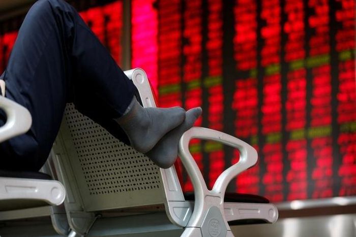 An investor puts his feet on a chair in front of an electronic board showing stock information at a brokerage house in Beijing, China, February 16, 2016.