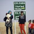 A Kurdish woman and her children stand by a sign for the village of Joldara (meaning plain covered in trees) and known as Shajra in Arabic, near the northeastern Syrian city of Qamishli on October 3, 2016