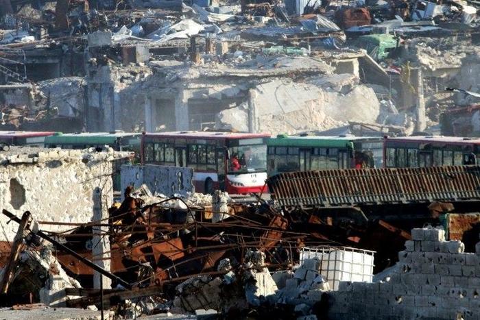 Buses drive through the Syrian government-controlled crossing of Ramoussa, on the southern outskirts of Aleppo, on December 18, 2016, during an evacuation operation of rebel fighters and civilians from rebel-held areas