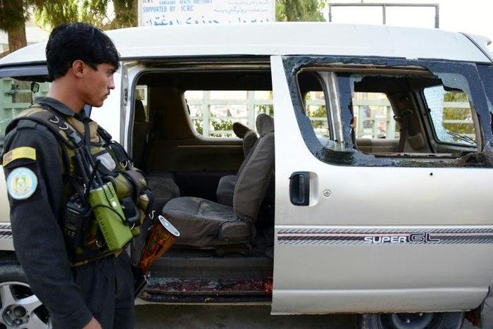 An Afghan policeman inspects a damaged vehicle in Kandahar on December 17, 2016, in which five female airport workers were killed