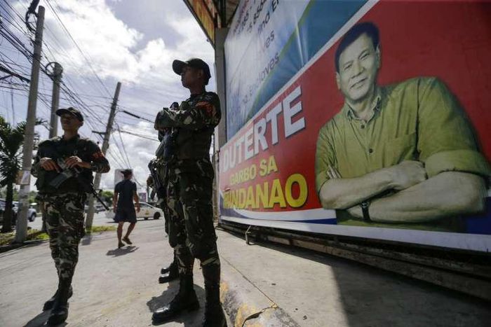 Filipino soldiers stand guard next to a poster of Philippine President Rodrigo Duterte.