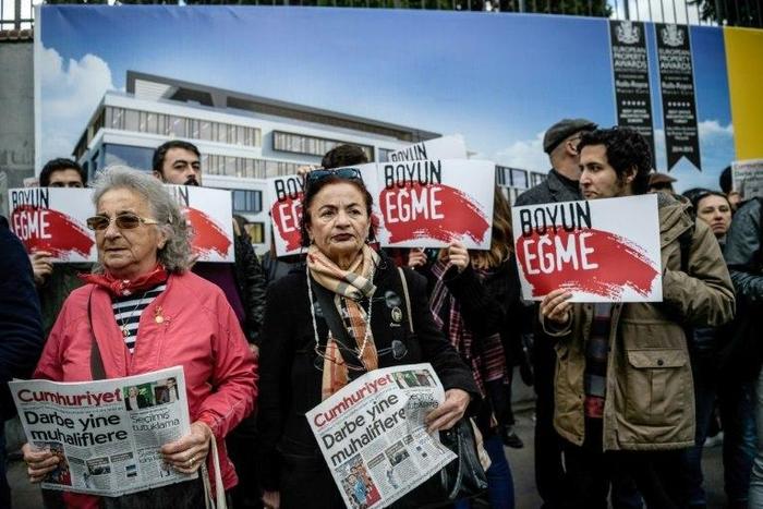 Protesters hold the Cumhuriyet daily newspaper, with the headline reading, "Coup against opposition", as others hold placards reading "Never submit" in front of the newspaper's headquarters on October 31, 2016 in Istanbul