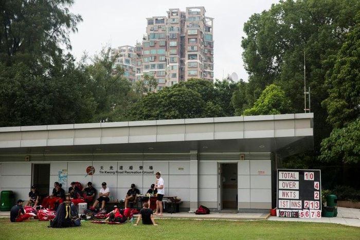 The Hong Kong Cricket Club rests during a lunch break of a cricket game on a small field among residential buildings in Hong Kong