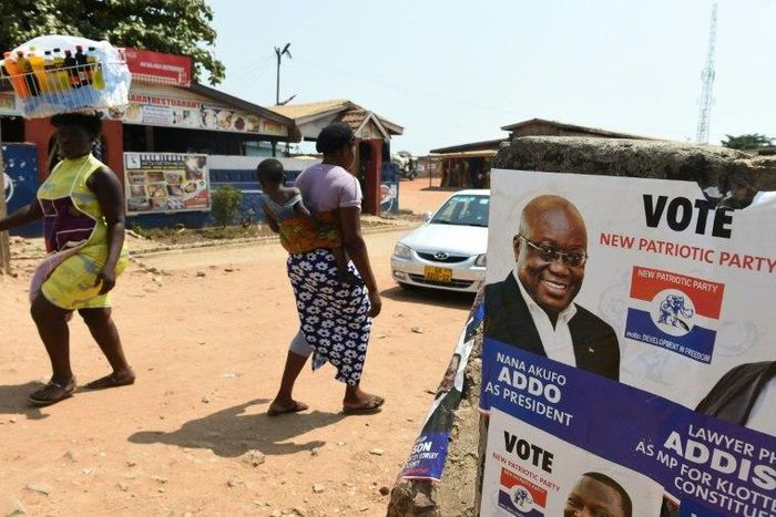 People walk past a campaign poster of presidential candidate of the opposition New Patriotic Party Nana Akufo-Addo in Accra, on December 3, 2016 ahead of the December 7 election
