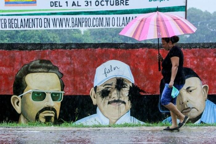 A woman passes by a graffiti depicting leaders of the revolution, including incumbent President Daniel Ortega (C), in San Jorge