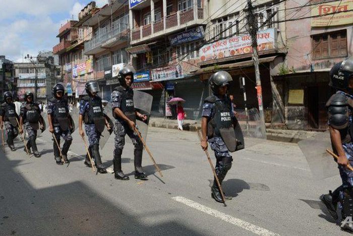 Nepalese police in riot gear walk past shuttered shops in Kathmandu.
