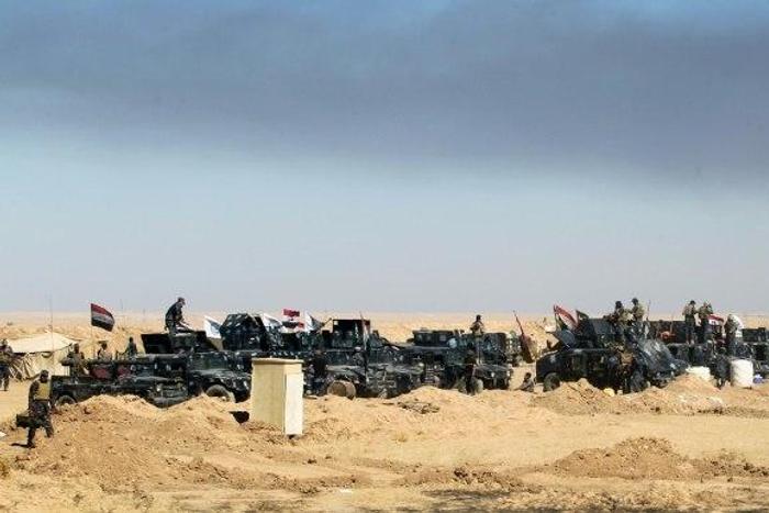 Smoke billows in the background as Iraqi forces gather at the Qayyarah military base, about 60 kilometres (35 miles) south of Mosul, as they prepare for an offensive to retake Mosul