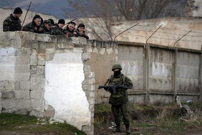 Ukrainian soldiers look on as an armed man, believed to be a Russian serviceman, stands guard at a Ukrainian military base in Perevalnoye in March 2014