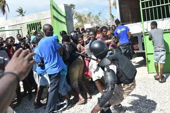 A Haitian policeman pushes back Hurricane Matthew victims waiting for the delivery of food from the UN's World Food Programme in Tobeck, in Les Cayes, in the south west of Haiti on October 13, 2016