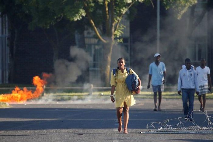 Students walk past a burning barricade as clashes between students and police erupt at the University of the Western Cape during protests demanding free tertiary education in Cape Town, South Africa, October 19, 2016.