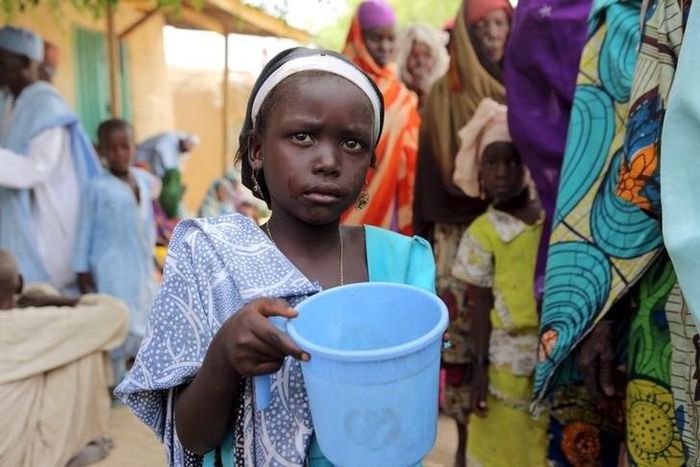 A girl drinks water as women queue for blankets and food given out by Nigerien soldiers in Damasak