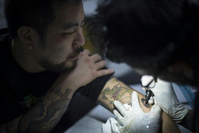 Tattoo artist Luke Satoru gets a number 9 tattooed on his arm by Manu Carrasco to commemorate the late Thai King Bhumibol Adulyadej, in Bangkok