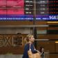 People pass a stock board showing stocks in red outside the Singapore Exchange in the central business district in Singapore August 12, 2015.
