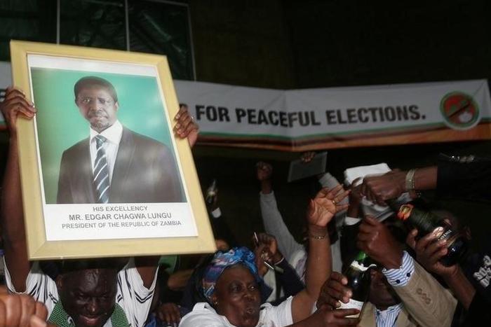 Patriotic Front General Secretary Davies Chama (L) celebrates while holding a portrait of President Edgar Chagwa Lungu after Lungu narrowly won re-election on Monday, in a vote his main rival Hakainde Hichilema rejected on claims of alleged rigging by ...
