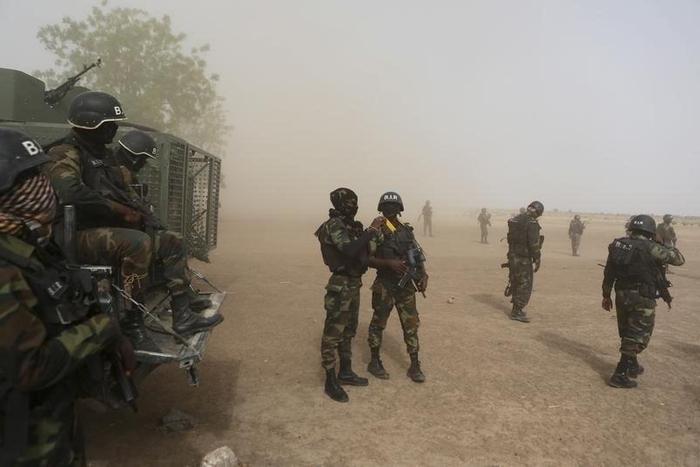 Cameroonian soldiers from the Rapid Intervention Brigade stand guard amidst dust kicked up by a helicopter in Kolofata, Cameroon, March 16, 2016.