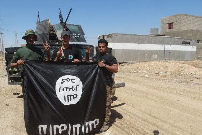 Iraqi security forces stand with an Islamic State flag which they pulled down in the town of Hit in Anbar province, April 2, 2016.