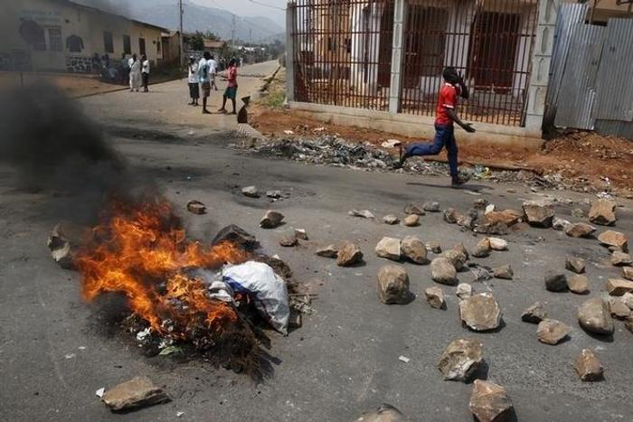 A man runs past a burning barricade on a rock strewn street in Bujumbura's Niyakabiga district on Presidential election day in Burundi, July 21, 2015.