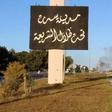 A sign which reads in Arabic, "The city of Sirte, under the shadow of Sharia" is seen as smoke rises in the background while forces aligned with Libya's new unity government advance on the eastern and southern outskirts of the Islamic State stronghold ...