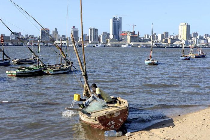 A fisherman cleans his boat beneath Maputo's skyline, Mozambique, August 15, 2015.
