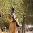 A member of a civilian vigilante group holds a hunting rifle while a woman pumps water into jerrycans in Kerawa, Cameroon, March 16, 2016.