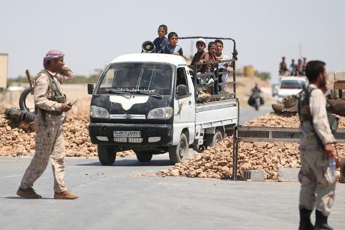 Syria Democratic Forces (SDF) fighters man a checkpoint as civilians on pick-up trucks evacuate from the southern districts of Manbij city after the SDF advanced into it in Aleppo Governorate, Syria, July 1, 2016.