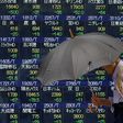 A pedestrian holding an umbrella walks past a stock quotation board outside a brokerage in Tokyo, Japan, June 13, 2016.
