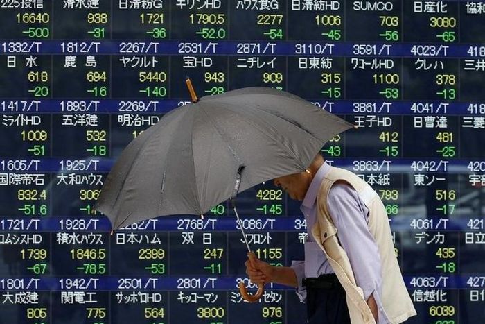 A pedestrian holding an umbrella walks past a stock quotation board outside a brokerage in Tokyo, Japan, June 13, 2016.