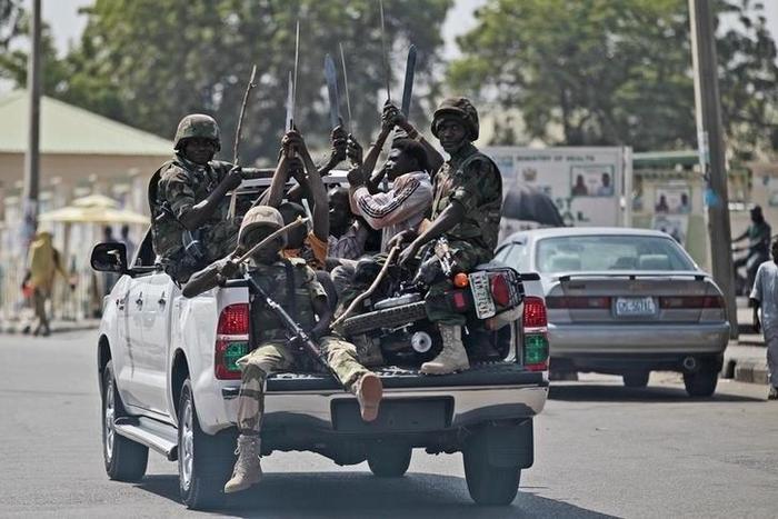 Soldiers and people carrying machetes ride on the back of a vehicle along a street in Gombe , Nigeria, January 30, 2015.