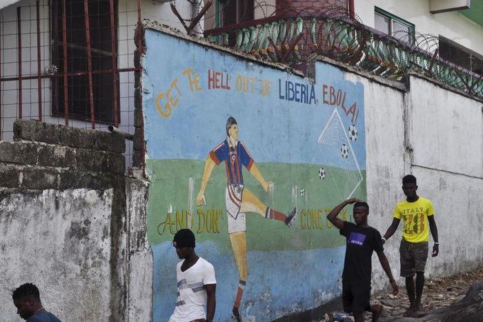 Men walk by a mural that reads "Get the hell of Liberia, Ebola! And don't come back" in Monrovia, Liberia, April 1, 2016. REUTERS/James Giahyue