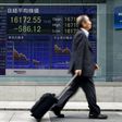 A man walks past an electronic board displaying the Nikkei average outside a brokerage in Tokyo, Japan, April 1, 2016.