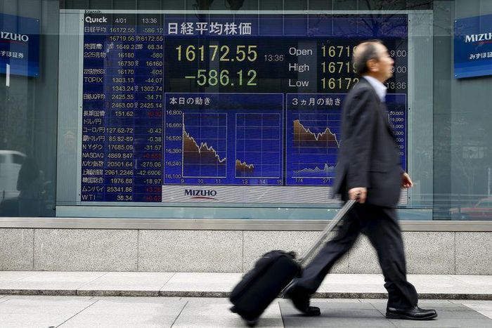 A man walks past an electronic board displaying the Nikkei average outside a brokerage in Tokyo, Japan, April 1, 2016.