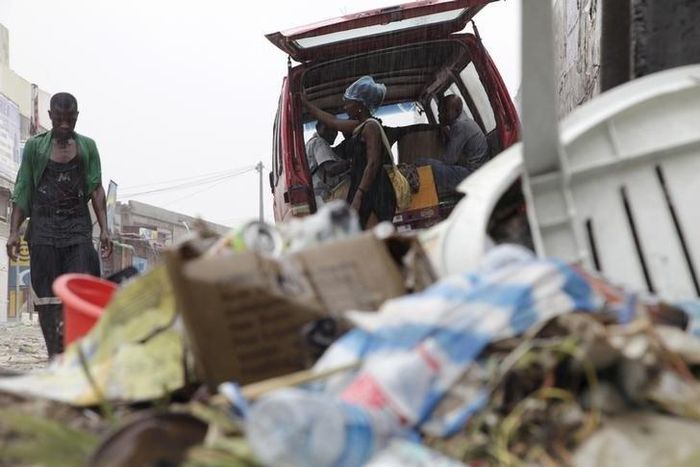 People walk past a pile of garbage along a street during rainfall, in Luanda, Angola, in this picture taken February 10, 2016.