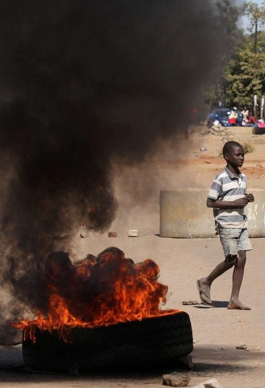 A boy walks past a burning tyre in Mufakose in Harare, Zimbabwe, July 6, 2016. REUTERS/Philimon Bulawayo