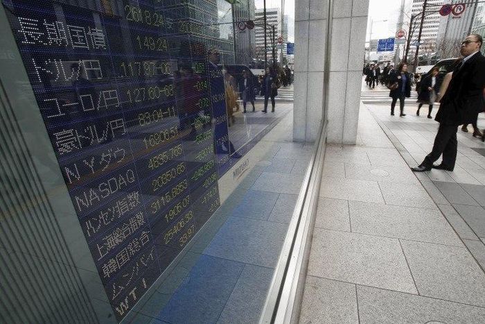 A pedestrian looks at an electronic board showing the exchange rates between (2nd top L to 4th) the Japanese yen against the U.S. dollar, the euro, and Australian dollar, and other market indices including Dow Jones and NASDAQ outside a brokerage in To...
