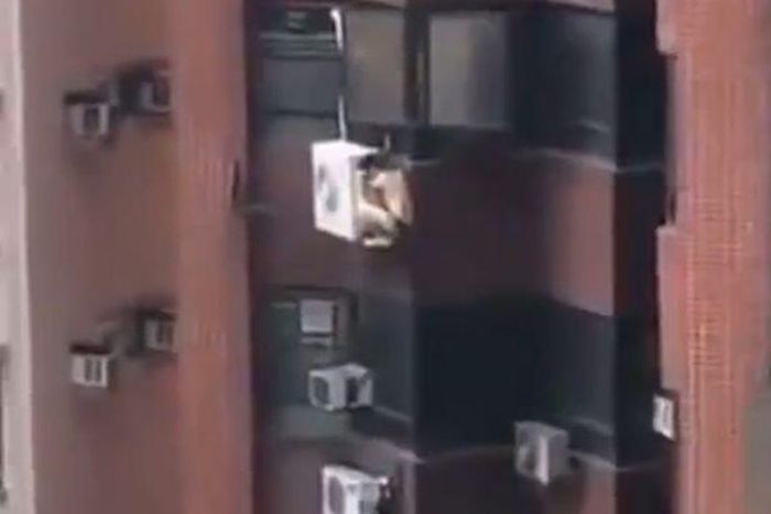 Naked man hanging on an air-condition machine.