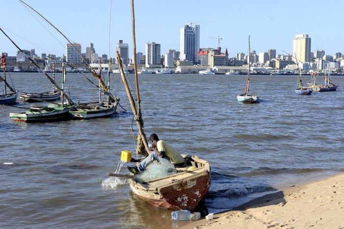 A fisherman cleans his boat beneath Maputo's skyline, Mozambique, August 15, 2015.