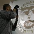 A photographer takes pictures through a glass carrying the International Monetary Fund (IMF) logo during a news conference in Bucharest , file.