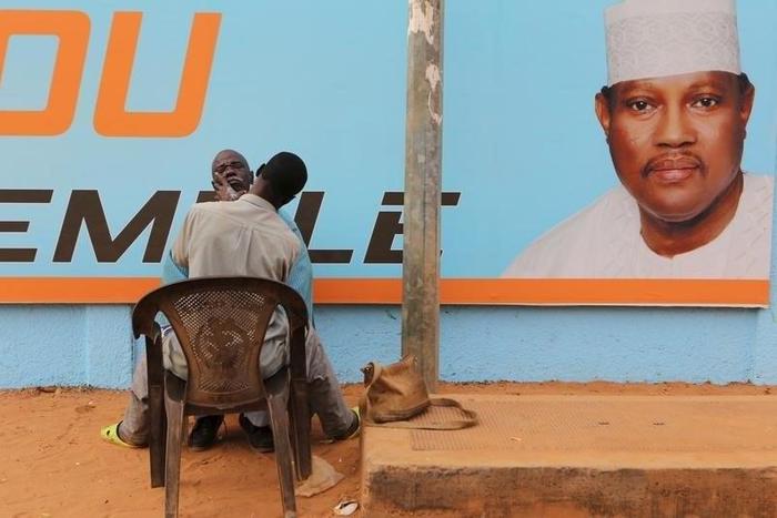 A man gets a haircut and a shave in front of a campaign poster of incarcerated opposition candidate Hama Amadou in Niamey, Niger, February 15, 2016. Niger holds presidential and legislative elections on Sunday.