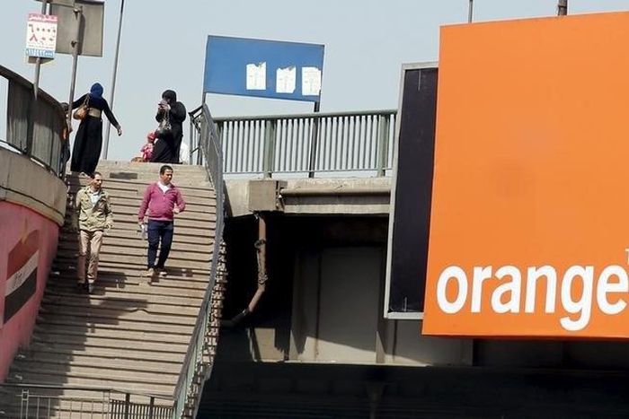 People walk past a sign of French telecom operator Orange hanging from a bridge in Cairo, Egypt March 13, 2016.