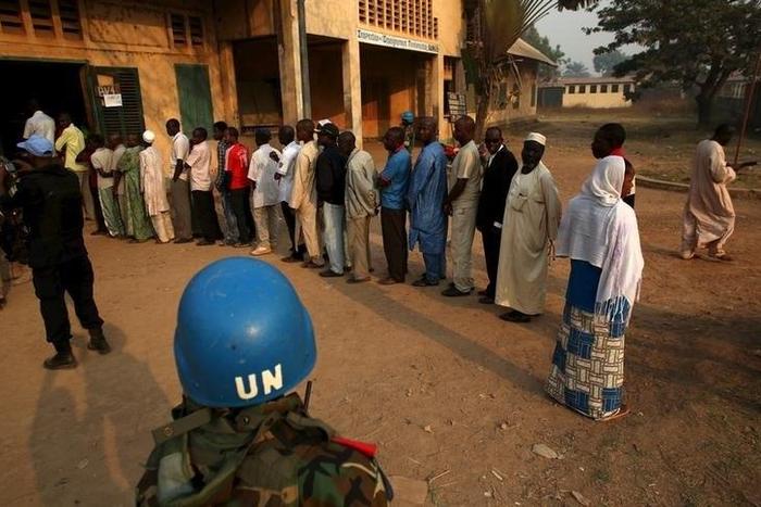 A United Nations security officer keeps guard as people wait in line to cast their votes during the second round of presidential and legislative elections in the mostly Muslim PK5 neighbourhood of Bangui, Central African Republic, February 14, 2016. RE...