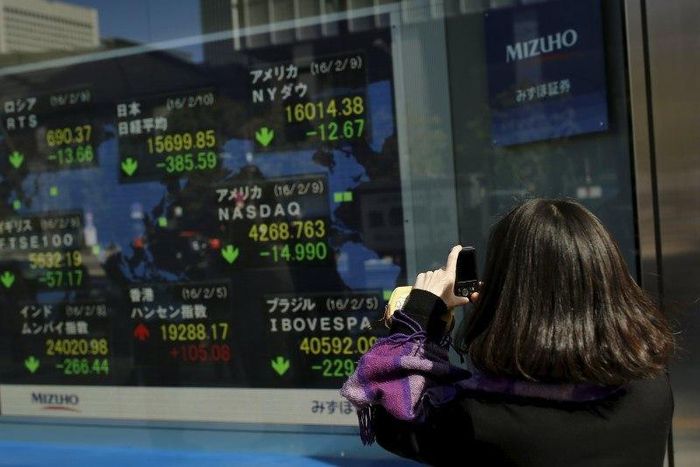 A woman takes pictures of a display showing market indices outside a brokerage in Tokyo, Japan, February 10, 2016. REUTERS/Thomas Peter