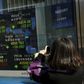 A woman takes pictures of a display showing market indices outside a brokerage in Tokyo, Japan, February 10, 2016. REUTERS/Thomas Peter
