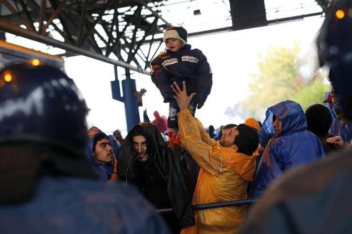 A migrant lifts a child as they wait to cross the border with Slovenia in Trnovec, Croatia October 19, 2015.   REUTERS/Antonio Bronic