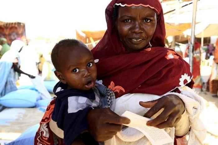 An internally displaced woman carries her child as she waits to receive food relief at a distribution center provided by the World Food Program at the Aboushouk camp in Al Fasher, North Darfur, Sudan, November 17, 2015. REUTERS/Mohamed Nureldin Abdalla...